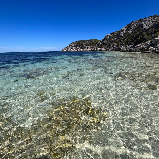 Photographic landscape of clear ocean waters, deep blue sky and rocks in the distance.
